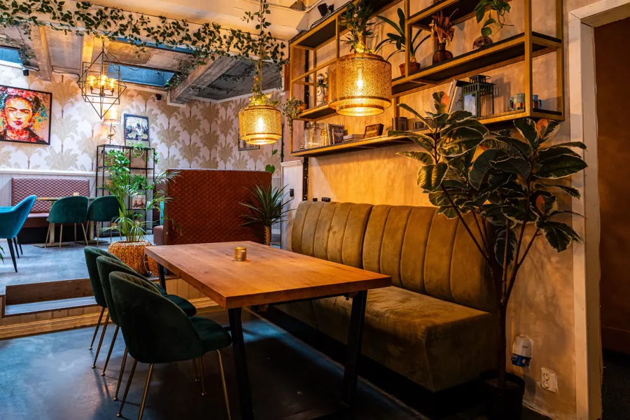 Velvet booth with a wooden table under gold lanterns and plants